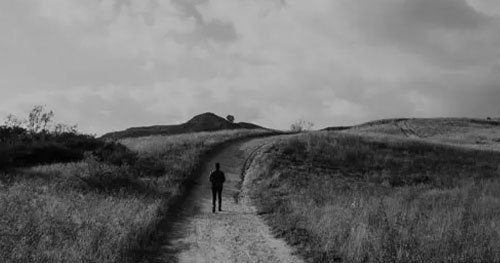man walking alone on long dirt road, lonelieness
