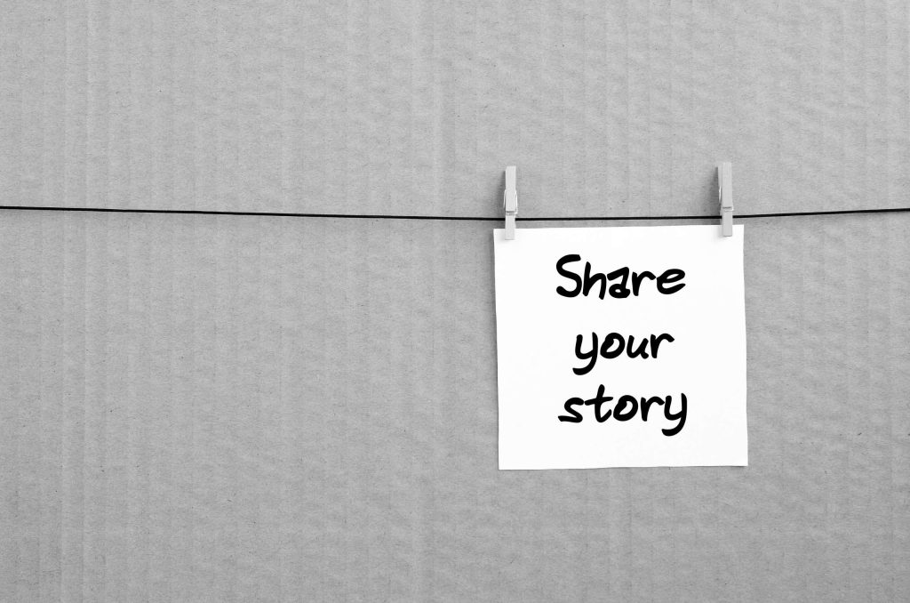 Share your story. Note is written on a white sticker that hangs with a clothespin on a rope on a background of brown cardboard