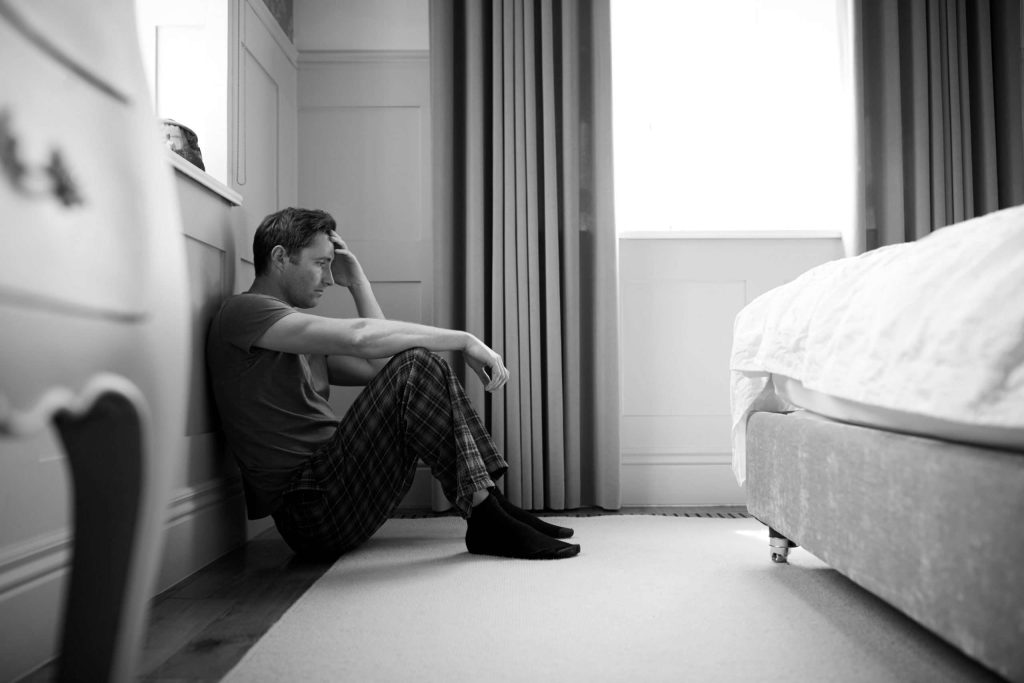 depressed man wearing pajamas sitting on floor