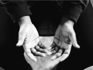 In black and white, two hands reach out, a gesture of offered help.