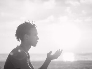 black and white image of man holding his hands up in prayer against the background of a sunrise