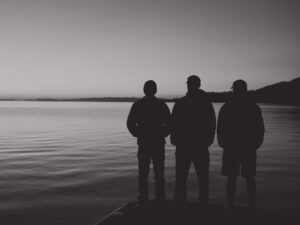 Three men standing together on the shore of a lake, in black and white